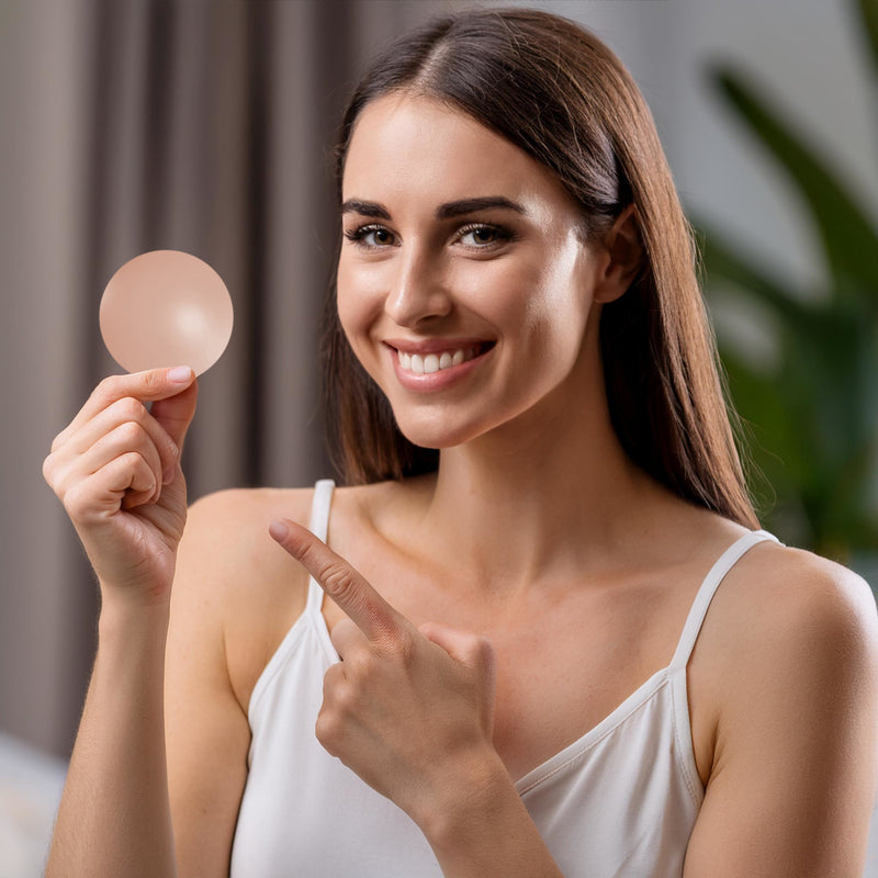 Uma mulher branca sorrindo com cabelo castanho segurando um cobre-mamilos Nip No More que combina perfeitamente com seu tom de pele. Pronta para conforto invisivel? Compre agora e sinta a confianca em qualquer look!